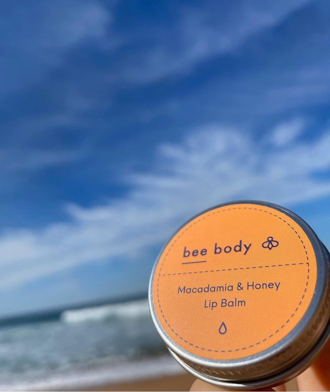 Macadamia & Honey Lip Balm: Embrace nature’s goodness with our soothing blend under a clear blue sky, set on a picturesque Australian beach.  