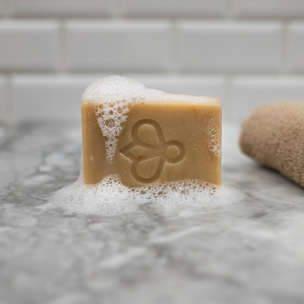 Honey Rose Soap - Resting on its side with refreshing suds, our soap infuses your bathroom with the delightful essence of honey and roses. Treat yourself to a luxurious bathing experience, as the enchanting aroma envelops your senses.